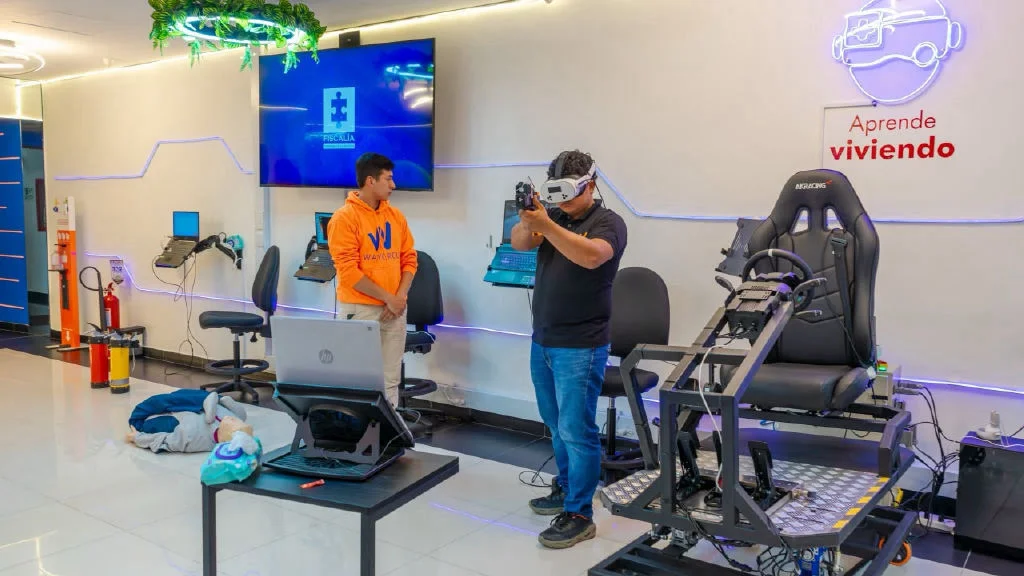 Sala HUB de WayGroup: un participante con visor de realidad virtual practica con un dispositivo de simulación junto a un instructor y una estación de conducción.